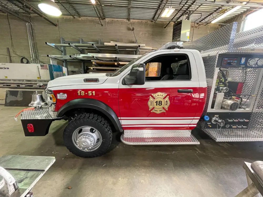 Exterior view of small fire truck showing cab, body compartments, and wheel/tire area.
